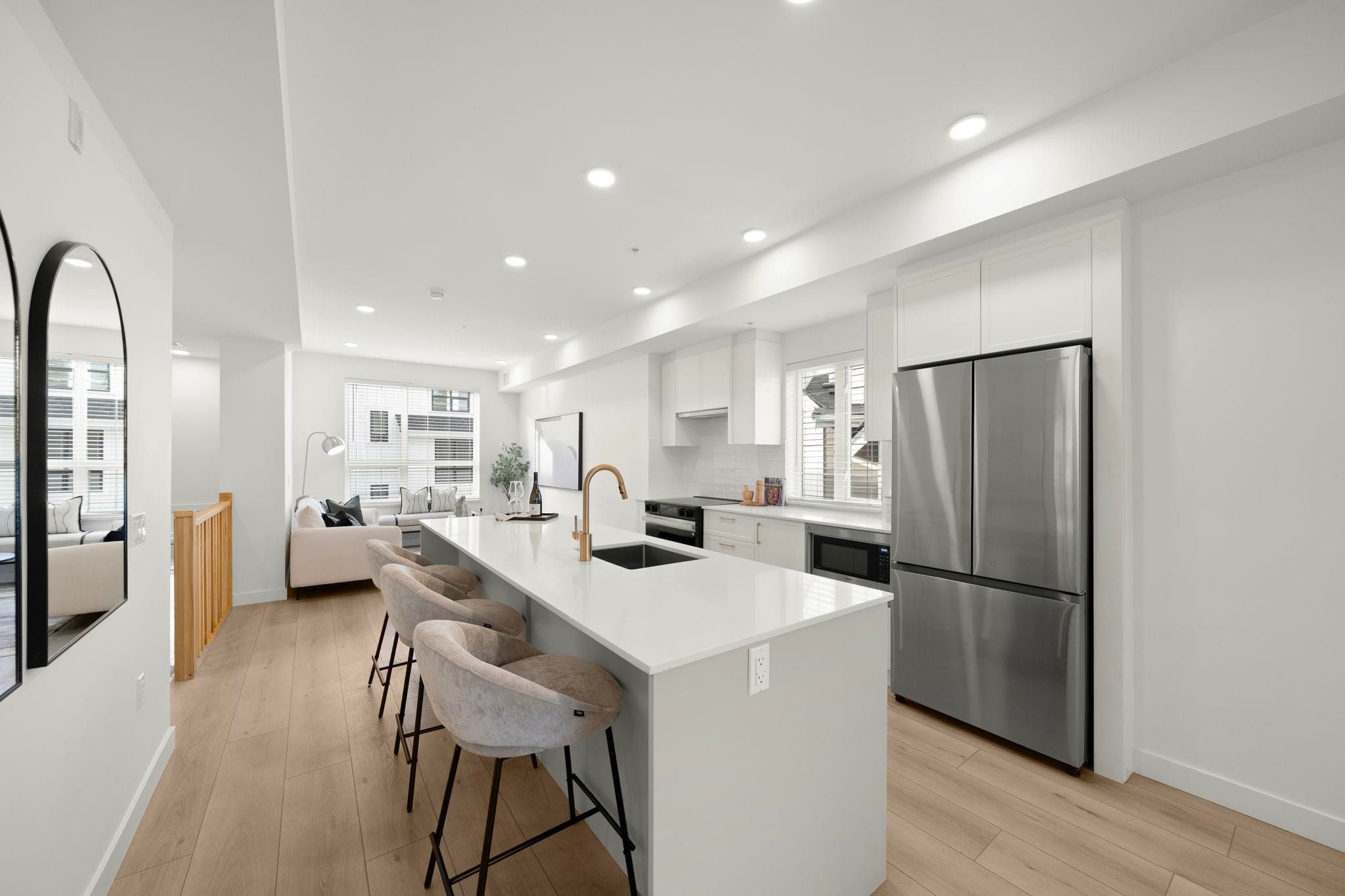 Kitchen at 6-728 Lea Avenue — white shaker cabinetry, quartz waterfall island, stainless steel refrigerator, and gold fixtures