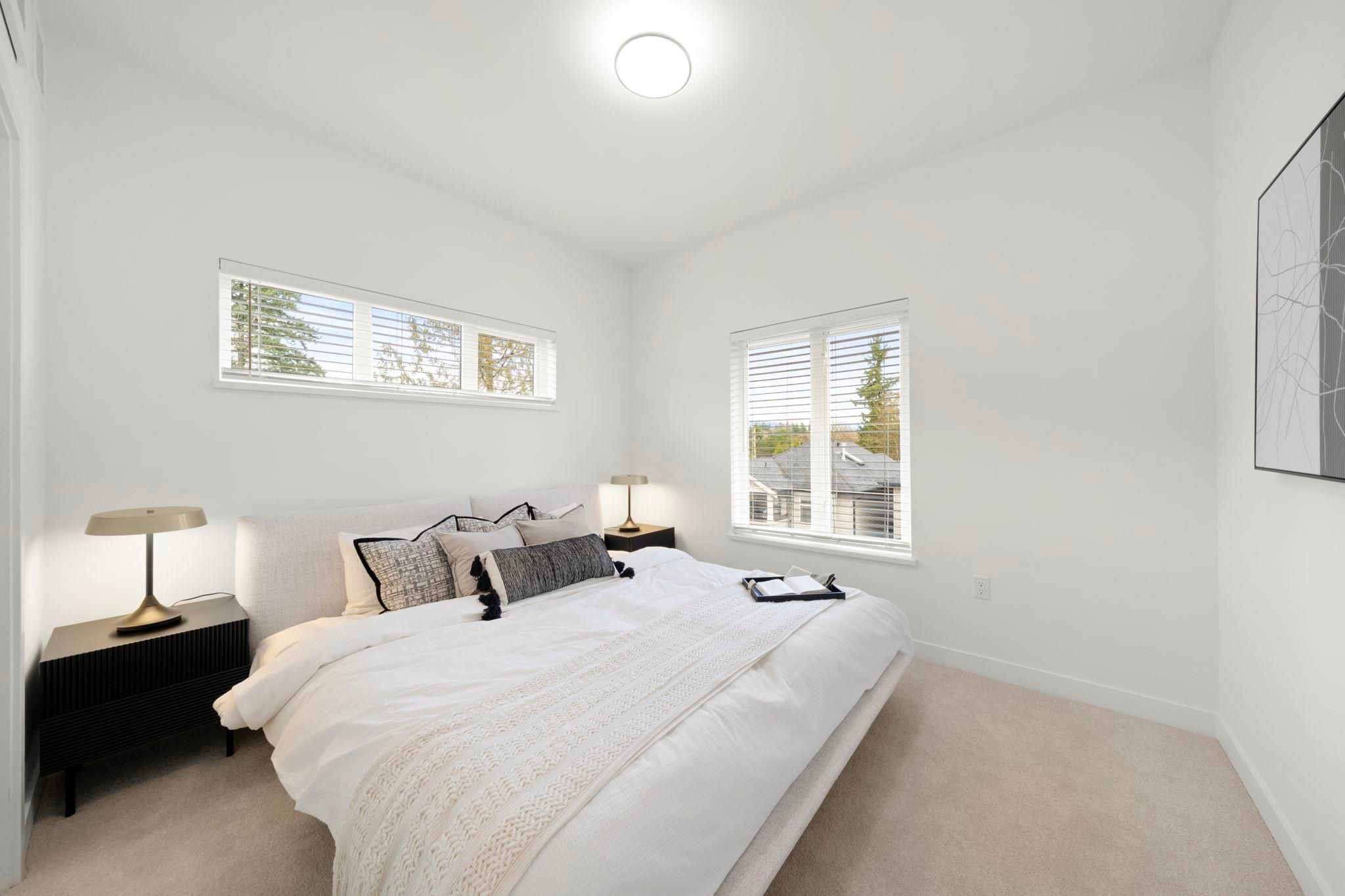 Primary bedroom at 6-728 Lea Avenue with upholstered bed, black nightstands, and dual windows looking out to the neighbourhood