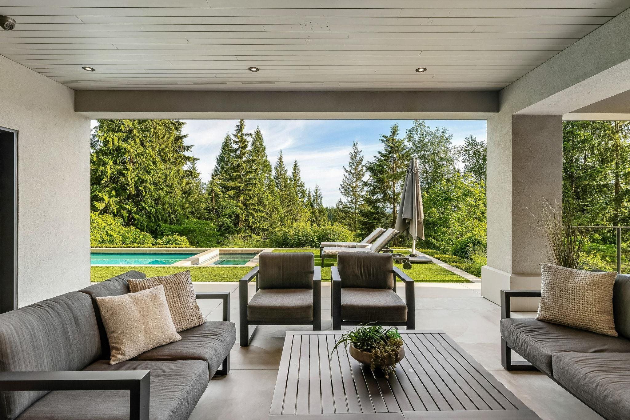 Covered outdoor living space with lounge seating overlooking the pool at Anmore estate