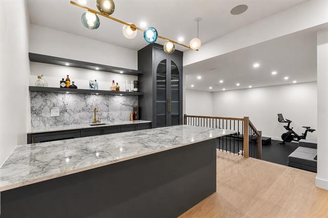 Wet bar with marble backsplash and glass cabinetry in the basement of 944 Caithness Crescent, Glenayre
