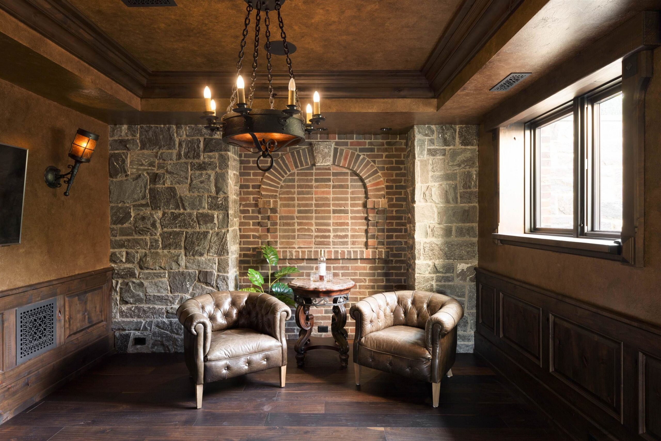 Stone-walled lounge with leather chairs and iron chandelier at Tannin Manor