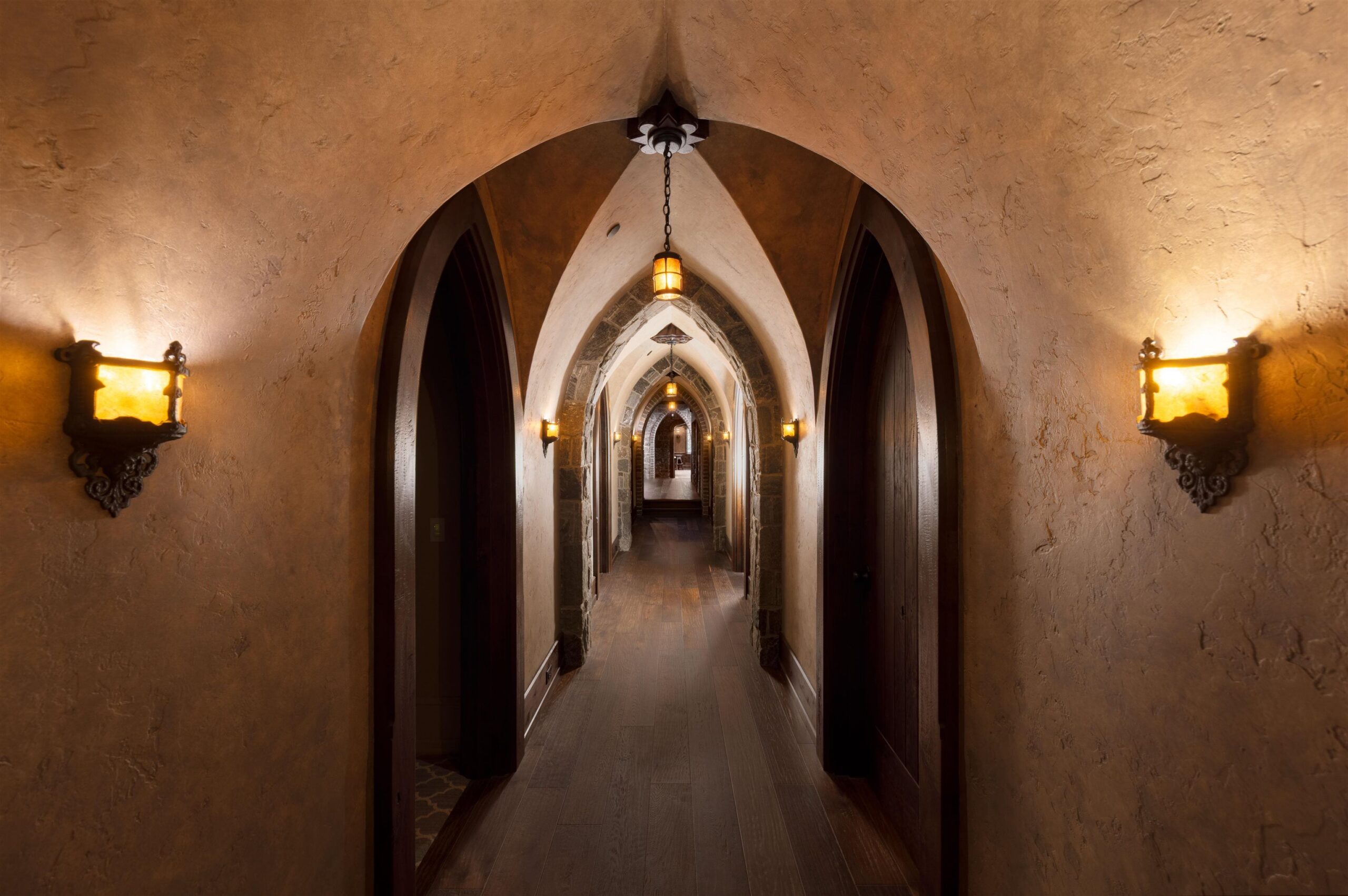 Arched plaster corridor with iron sconces inside Tannin Manor