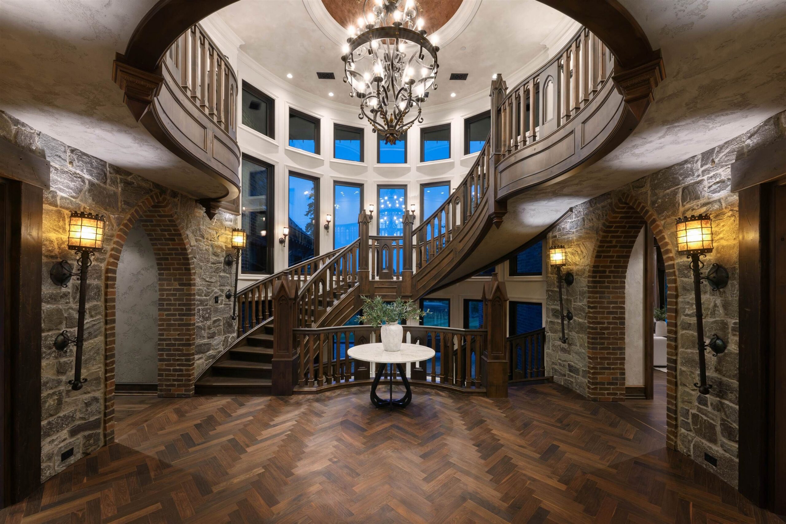 Grand foyer with curved staircase, stone walls and iron chandelier at Tannin Manor